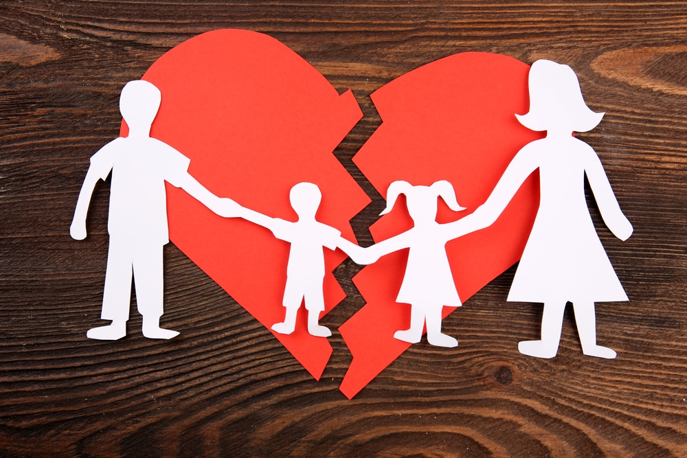 paper cutout silhouette of a family split apart on a paper heart to symbolise divorce